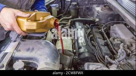 Mechaniker, der das Öl in einem Auto auffüllend, ein Pint Öl durch einen Trichter in den Motor gießt, Nahaufnahme seiner Hände und des Öls Stockfoto