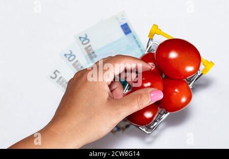 Schuss von Tomaten in Warenkorb isoliert auf weißem Hintergrund mit Euro-Scheine darunter und Weiblichkeit Hand nach Tomaten greifen. Draufsicht. Reif lecker rot Stockfoto