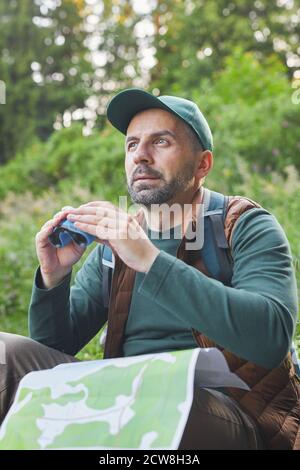 Vertikales Porträt eines reifen Mannes mit Fernglas und Karte während Wandern allein im Wald Stockfoto