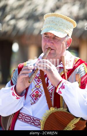08 29 2020 Weißrussland, Ljaskowitschi. Feier in der Stadt. Ein älterer slawischer Mann in Nationaltracht spielt die Pfeife. Stockfoto