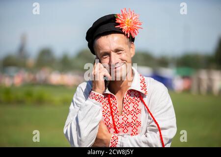 08 29 2020 Weißrussland, Ljaskowitschi. Feier in der Stadt. Ein älterer slawischer Mann in einem bestickten Hemd spricht am Telefon. Stockfoto