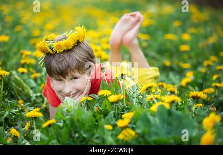 Ein fröhlicher Junge mit einem Löwenzahnkranz liegt auf dem Gras. Kind auf der Wiese. Stockfoto