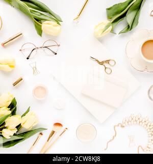 Weiblicher Arbeitsplatz mit gelben Tulpenblüten, Damenmode goldene Accessoires, Tagebuch, Gläser auf weißem Hintergrund. Flach liegend. Draufsicht Hintergrund. Stockfoto