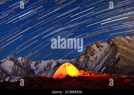 Herrliche Aussicht mit Sternentouren über die Berge; orange aufgehelltes Zelt unter dem Nachthimmel als Reisekonzept Stockfoto