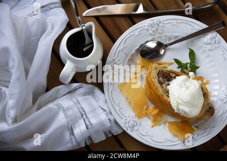 apfelstrudel mit einer Kugel Vanilleeis, Minze auf einer weißen Glasplatte. Stockfoto