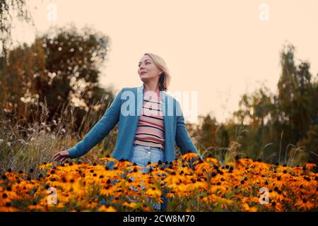 Blonde kaukasische Weibchen mit bob Haarschnitt stehen im Herbst Feld zwischen orangen Blumen mit ausgebreiteten Händen. Stockfoto