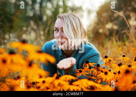 Blonde kaukasische Frau mit bob Haarschnitt Schläge Kuss. Herbst Frau Porträt mit leuchtend orange Blumen Stockfoto