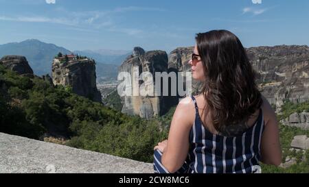 Die malerische Aussicht von der Meteora, Griechenland. Mädchen sitzt auf dem Felsen, Kloster der Heiligen Dreifaltigkeit im Hintergrund. Stockfoto