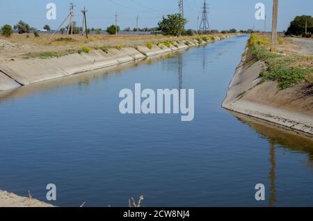 Bewässerung landwirtschaftlichen Kanal mit Wasser. Stromleitung entlang des Kanals für die Bewässerung. Sommer sonnigen Tag. Agrarindustrie. Stockfoto