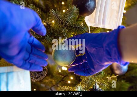 Person schmückt einen schönen Weihnachtsbaum mit Schutzhandschuhen für Covid-19, Konzept für Coronavirus und Weihnachtsfeiertag Stockfoto