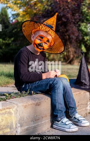 Halloween Kinder. Portrait lachender Junge mit Kürbis Gesichtsmaske im Hexenkostüm Hut mit Süßigkeiteneimer auf der Straße Stockfoto