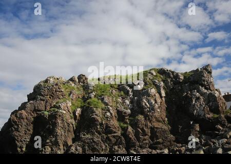 Dunure, Ayrshire, Schottland, UK.EIN Felsvorsprung mit Gras bedeckt mit blauem Himmel und weißen Wolken Stockfoto