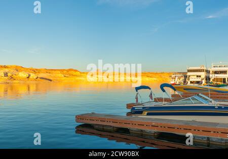 Als Sonnenuntergänge Licht trifft die Felsen Böschungen mit einem goldenen Glühen Sie über die andere Seite Lake Powell von Marina Liegeplätze mit Vergnügungsboote auf künstlichen Reservo Stockfoto