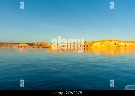 Als Sonnenuntergänge Licht trifft die Felsen Böschungen mit einem goldenen Glow auf der anderen Seite Lake Powell ein künstlich anmuttes Reservoir Der Colorado River in Utah und Arizona Stockfoto