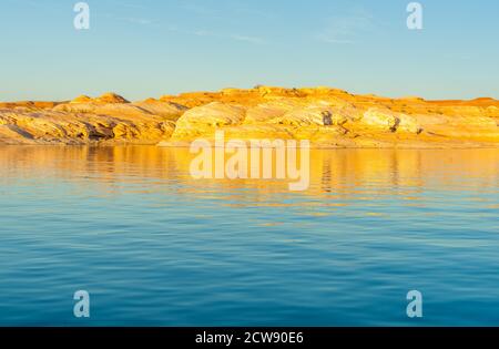 Als Sonnenuntergänge Licht trifft die Felsen Böschungen mit einem goldenen Glow auf der anderen Seite Lake Powell ein künstlich anmuttes Reservoir Der Colorado River in Utah und Arizona Stockfoto