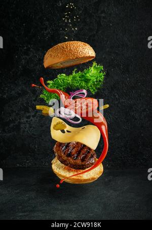 Hamburger mit schwebenden Zutaten auf dunklem Hintergrund. Kreatives Stillleben Konzept und Werbung Stockfoto