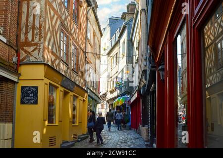 Touristen gehen in einer malerischen Seitenstraße an Fachwerkbaugeschäften im mittelalterlichen Küstenfischerdorf Honfleur in der Normandie vorbei Stockfoto