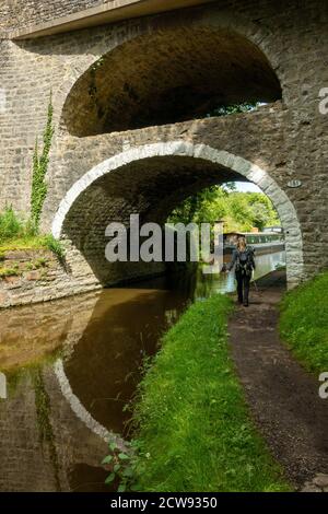 Walker nähert sich der doppelbögigen Kanalbrücke Nr. 161 bei East Marton auf dem Leeds Liverpool Kanal mit der A59 über der Spitze, North Yorkshire, UK Stockfoto