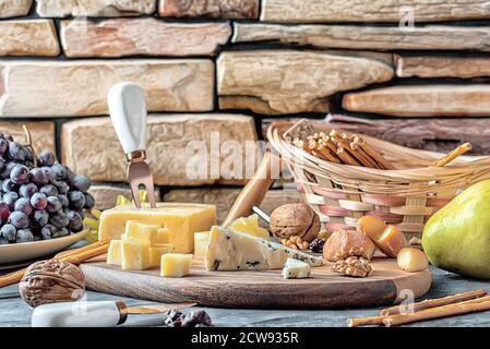 Käseplatte aus verschiedenen Käsesorten - Emmentaler, hausgemachte, Parmesan, Blauschimmelkäse, Brotscheiben, Walnüsse, Rosinen, Birne, Trauben auf schwarzem Tisch Stockfoto