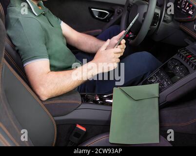 Ein junger Mann mit einem Tablet in der Hand am Sportwagen. Multitasking Stockfoto