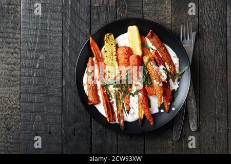 Salat aus gerösteten Karotten mit Joghurt, Gewürzen und Kräutern auf dunklem Grund. Stockfoto