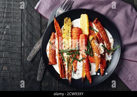 Salat aus gerösteten Karotten mit Joghurt, Gewürzen und Kräutern auf dunklem Grund. Stockfoto