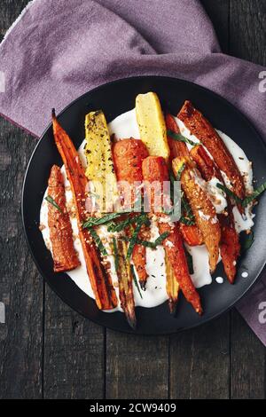 Salat aus gerösteten Karotten mit Joghurt, Gewürzen und Kräutern auf dunklem Grund. Stockfoto