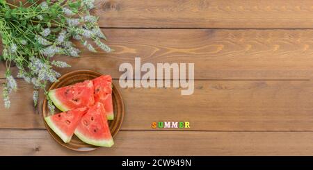 Vier Scheiben reife Wassermelone auf einem Teller und ein Bouquet von blühendem Oregano. Brauner Holztisch. Der Blick von oben. Speicherplatz kopieren. Banner Stockfoto