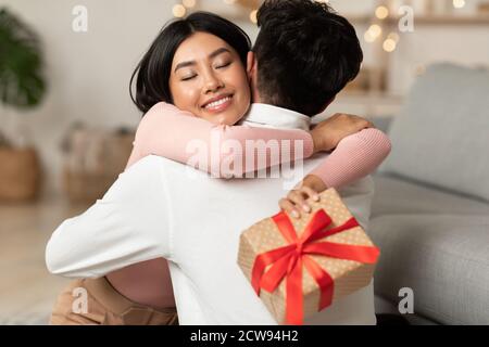 Fröhlich Asiatische Freundin Umarmt Freund Holding Verpackt Geschenkbox Im Innen Stockfoto