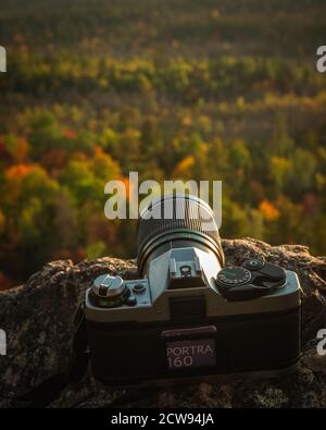 Eine 35-mm-Kamera mit Kodak Portra 160 Film sitzt auf einem Felsen am Rande einer Klippe in Ontario, Kanada, ausgerichtet auf einen Wald von herbstlichen Bäumen belo Stockfoto