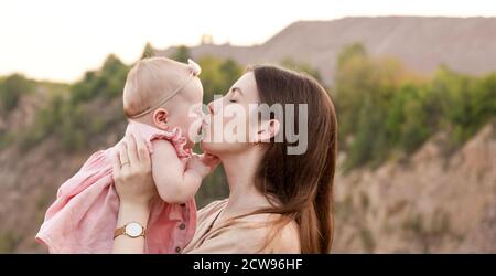 Mama hält ein Kind in den Armen und küsst ihn sanft auf die Wange draußen. Mutter und Tochter. Familienkonzept. Stockfoto