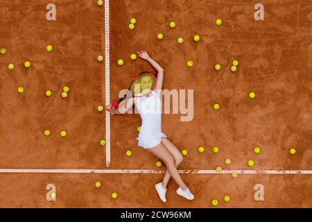 Portrait von lächelndem Mädchen entspannen auf dem Tennisplatz mit einer Menge Bälle und Schläger nach harten Tennis trainingg im Freien. Dolly-Schuss. Draufsicht. Stockfoto