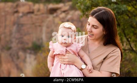 Glückliche junge Mutter hält ihre kleine Tochter im Freien in den Armen. Mama lächelt und sieht ihre Tochter an. Stockfoto