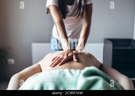 Eine Frau Physiotherapeutin, die eine Rückenmassage für einen Mann in der Arztpraxis macht. Nahaufnahme der Hände beim Massieren. Stockfoto