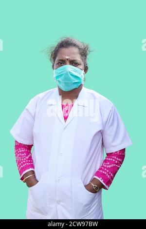 Ein Arzt trägt eine Maske und Hand in seinem Weiße Manteltasche auf blauem Hintergrund Stockfoto