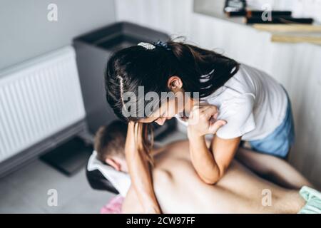 Eine Frau Physiotherapeutin, die eine Rückenmassage für einen Mann in der Arztpraxis macht. Nahaufnahme der Hände beim Massieren. Stockfoto