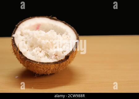 Kokosnüsse mit Kokosflocken sind auf einem Holztisch isoliert Auf schwarzem Hintergrund Stockfoto
