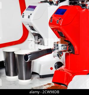 Die leuchtend rote Kaffeemühle mahlt die gerösteten Bohnen zu Pulver. Der frisch gemahlene Kaffee wird im Portafilter gestreut. Stockfoto