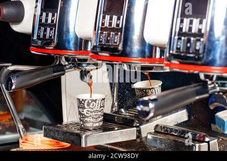 Bei der Zubereitung von aromatischem Kaffee gießt die Kaffeemaschine den Kaffee in eine Pappbecher. Stockfoto