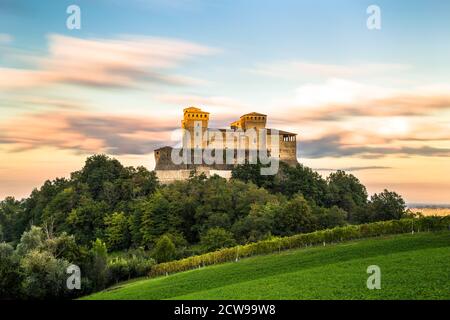 Einzigartige Langzeitansicht von Torrechiara Burg auf der Spitze der grünen Weinrebe Feld während eines bewölkten Sonnenuntergangs, Parma, Italien Stockfoto