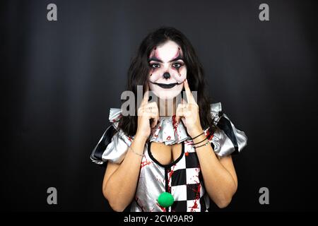 Frau in einem halloween Clown Kostüm über isoliertem schwarzem Hintergrund Lächelnd selbstbewusst zeigen und zeigen mit den Fingern Zähne und Mund Stockfoto