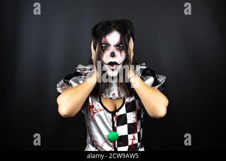 Frau in einem halloween Clown Kostüm über isolierten schwarzen Hintergrund verrückt und mit Händen auf dem Kopf verängstigt, Angst und überrascht von Schock Stockfoto