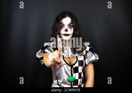 Frau in einem halloween Clown Kostüm über isoliertem schwarzem Hintergrund Zeigt und zeigt mit den Fingern Nummer eins nach oben, während ist Ernst Stockfoto