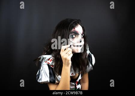 Frau in einem halloween Clown Kostüm über isoliertem schwarzem Hintergrund Blick durch eine Lupe Stockfoto