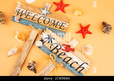 Holzschilder begrüßen Strand, Seesterne und Muscheln auf gelbem Hintergrund. Stockfoto