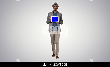 Casual Mann in einem Hut zu Fuß und zeigt digitale Tablette Zur Kamera Stockfoto