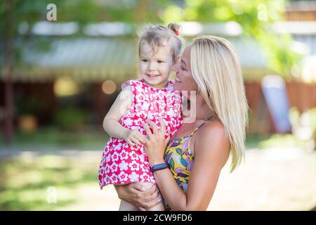 Schöne junge Frau hält kleine Mädchen im Park, Mutter und Tochter lachen und reden auf Spaziergang im Park Stockfoto