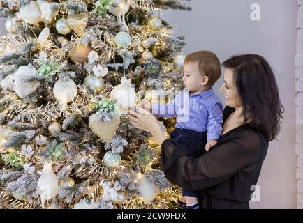 Attraktive reife Frau zeigt Kugeln auf Weihnachtsbaum zu ihr Baby Enkel zu Hause Stockfoto