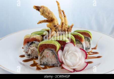 Würziger Thunfisch und frittierte Tempura in Sushi-Rolle mit kunstvoller Rettichblüte auf einem Teller zum Essen. Stockfoto