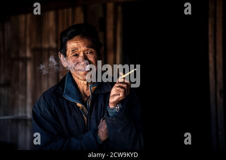 Chiang Mai / Thailand - Jan 16 2016 : der alte Asiate raucht und lächelt mit guter Laune, trägt alte Kleider, ein Bergstämmier in einem ländlichen Dorf in Nort Stockfoto